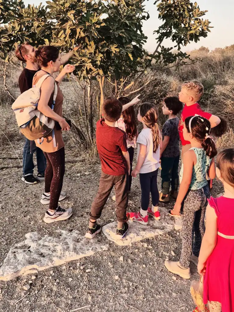 נטע מסבירה לקבוצת ילדים על רקע עץ תאנה